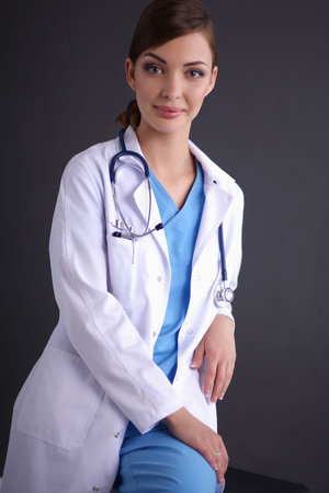Beautiful female doctor sitting  on stool isolated grey backgroundの写真素材