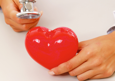 Female doctor examining a red heart with a stethoscopeの写真素材