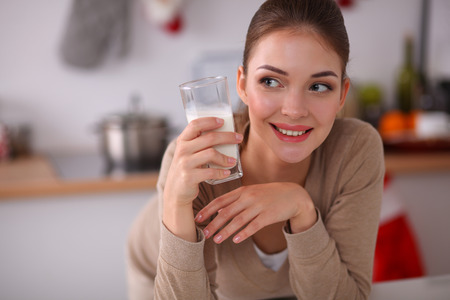 Smiling young woman drinking milk, standing in the kitchenの写真素材