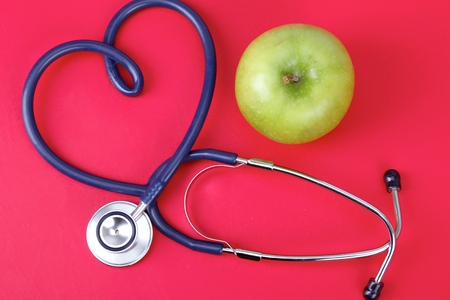 Green apple and stethoscope isolated on red background.の写真素材