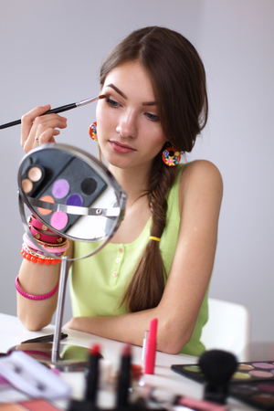 Young beautiful woman making make-up near mirror,sitting at the deskの写真素材