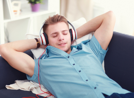 Man listening music in headphone on the sofa at homeの写真素材