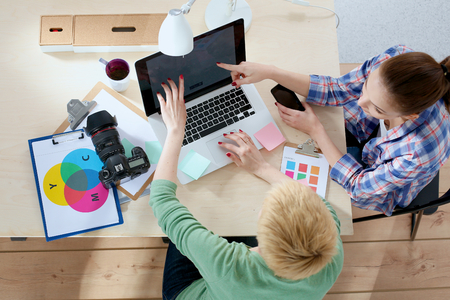 Two women photographer sitting on the desk with laptopの写真素材