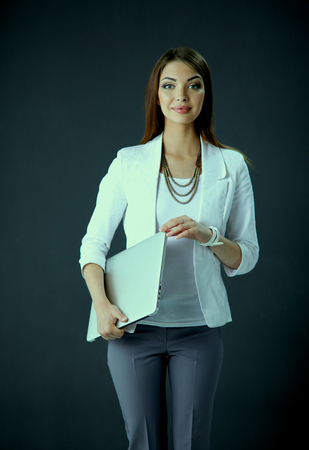 Young woman holding a laptop, standing on gray backgroundの写真素材