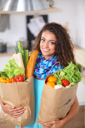 Young woman holding grocery shopping bag with vegetables . Standing in the kitchen.の写真素材