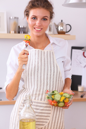 Young woman eating fresh salad in modern kitchen .の写真素材