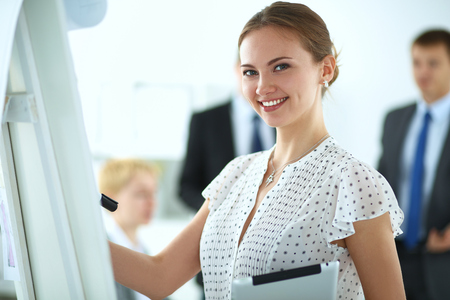 Businesswoman writing on flipchart while giving presentation to colleagues in office .の写真素材