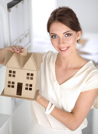 Portrait of female architect holding a little house, standing in office.の写真素材