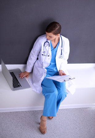 Beautiful nurse holding folder and taking notes - sitting on grey backgroundの写真素材