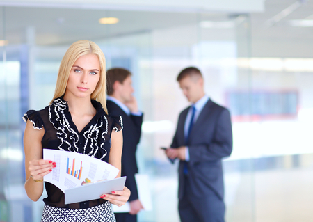 Business woman standing in foreground with a folder in her hands .の写真素材