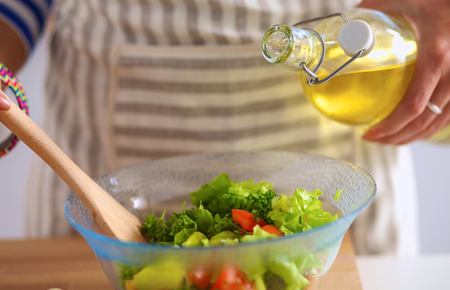 Young woman mixing fresh salad, standing near desk .の写真素材