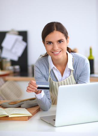 Woman online shopping using computer and credit card in kitchenの写真素材