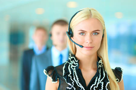 Portrait of beautiful business woman in headphones smiling with colleagues in backgroundの写真素材