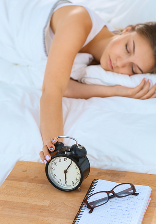 A young woman putting her alarm clock off in the morningの写真素材