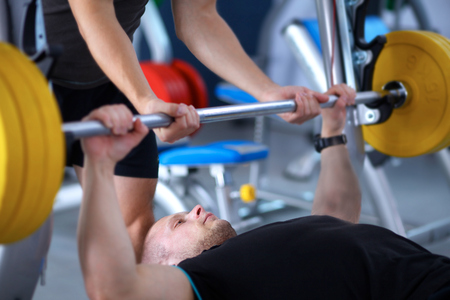 Young man lifting the barbell in the gym with instructor .の写真素材
