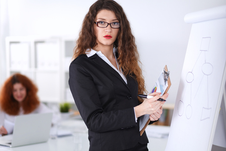 Young woman standing near board with folder, in officeの写真素材