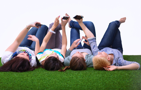 Four young women lying on green grass with mobile phone  .の写真素材