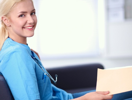 Closeup portrait of a happy young doctor sitting on the sofa with folderの写真素材