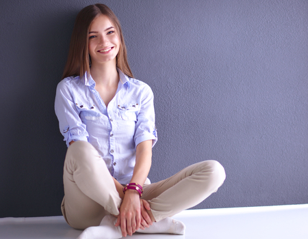 Portrait of young woman sitting on the floor near dark wallの写真素材