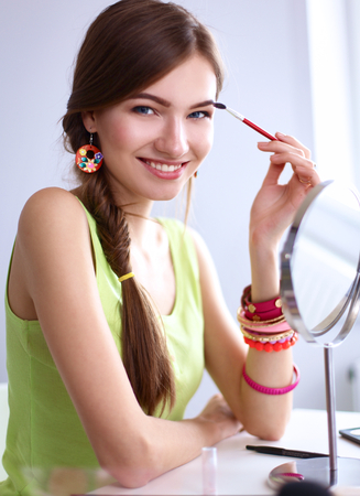 Young beautiful woman making make-up near mirror,sitting at the desk.の写真素材