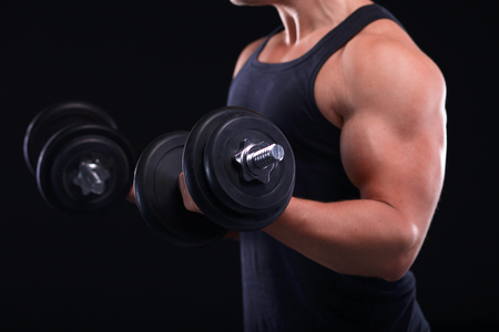 Handsome muscular man working out with dumbbells isolated on black backgroundの写真素材