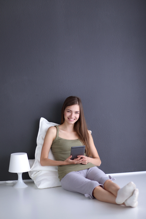 Portrait of a pretty brunette woman sitting on the floor with a pillow and plane tableの写真素材
