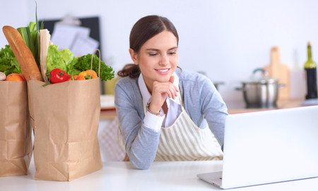 Beautiful young woman cooking looking at laptop screen with receiptの写真素材