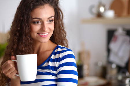 Portrait of young woman with cup against kitchen interiorの写真素材