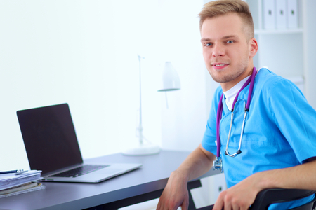 Portrait of a smiling male doctor with laptop sitting at deskの写真素材