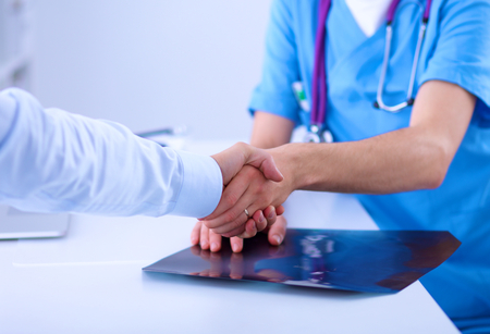 Doctor shaking hands with a patient, sitting on the deskの写真素材