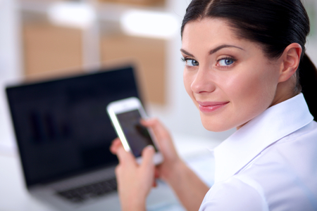 Businesswoman sending message with smartphone in officeの写真素材