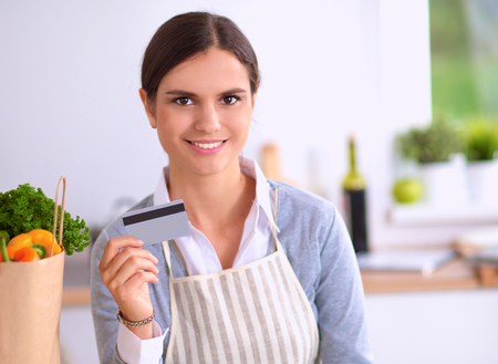 Woman online shopping using computer and credit card in kitchenの写真素材
