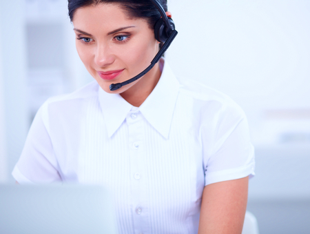 Portrait of beautiful business woman working at her desk with headset and laptopの写真素材