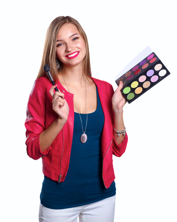 Young beautiful woman holds in one hand and a palette with paint and shadows for makeup, second hand brush for makeup.の写真素材
