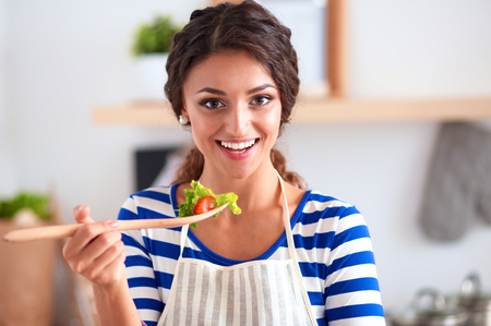 Young woman eating fresh salad in modern kitchen, isolatedの写真素材