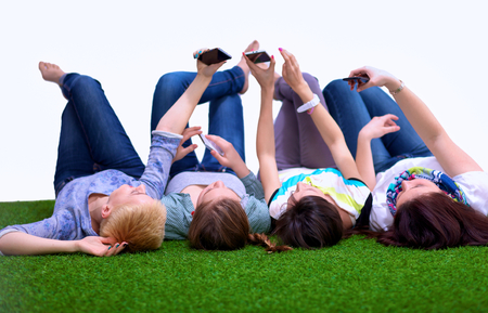 Four young women lying on green grass with mobile phone  .の写真素材
