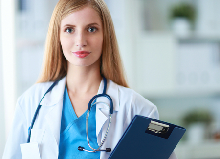 Portrait of woman doctor with stethoscope at hospital corridor, holding a folderの写真素材