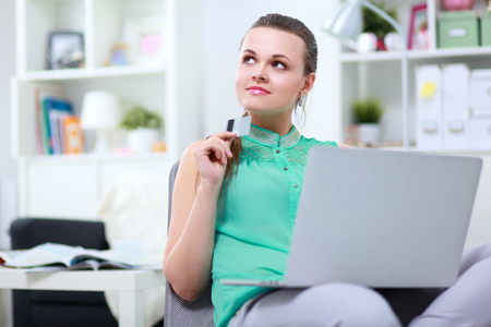 Smiling woman with documents sitting on the desk with laptopの写真素材
