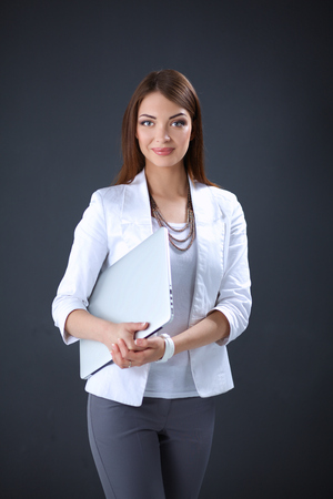 Young woman holding a laptop, standing on gray background.の写真素材