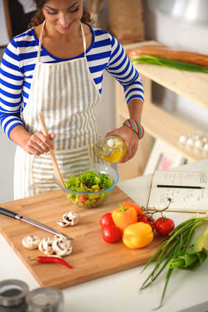Young woman mixing fresh salad standing near deskの写真素材