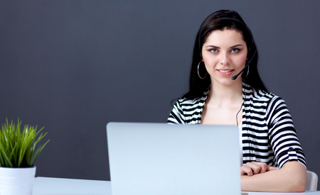 Portrait of beautiful business woman working at her desk with headset and laptopの写真素材