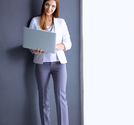 Young woman holding a laptop, standing on gray background.の写真素材
