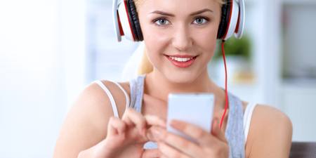 Portrait of young beautiful woman at home sitting on sofa and listening musicの写真素材