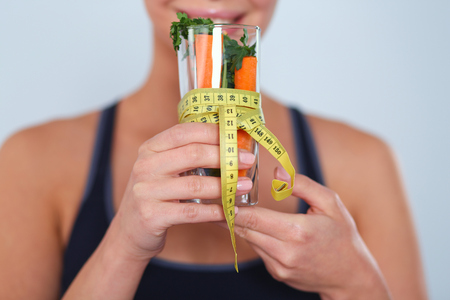 Woman holding a drinking glass full of fresh fruit salad with a tape measure around the glass.の写真素材