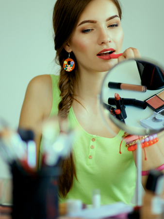 Young beautiful woman making make-up near mirror,sitting at the desk.の写真素材