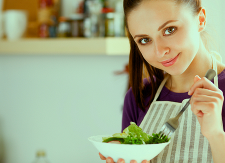 Young woman eating fresh salad in modern kitchen .の写真素材