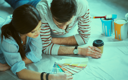 Couple choosing paint colour from swatch for new home lying on wooden floor.の写真素材
