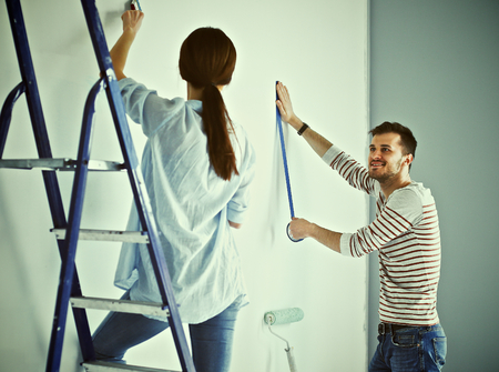 Portrait of happy smiling young couple  painting interior wall of new house.の写真素材