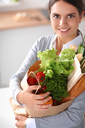 Young woman holding grocery shopping bag with vegetables . Standing in the kitchen.の写真素材