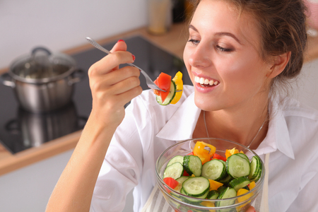 Young woman eating fresh salad in modern kitchen .の写真素材